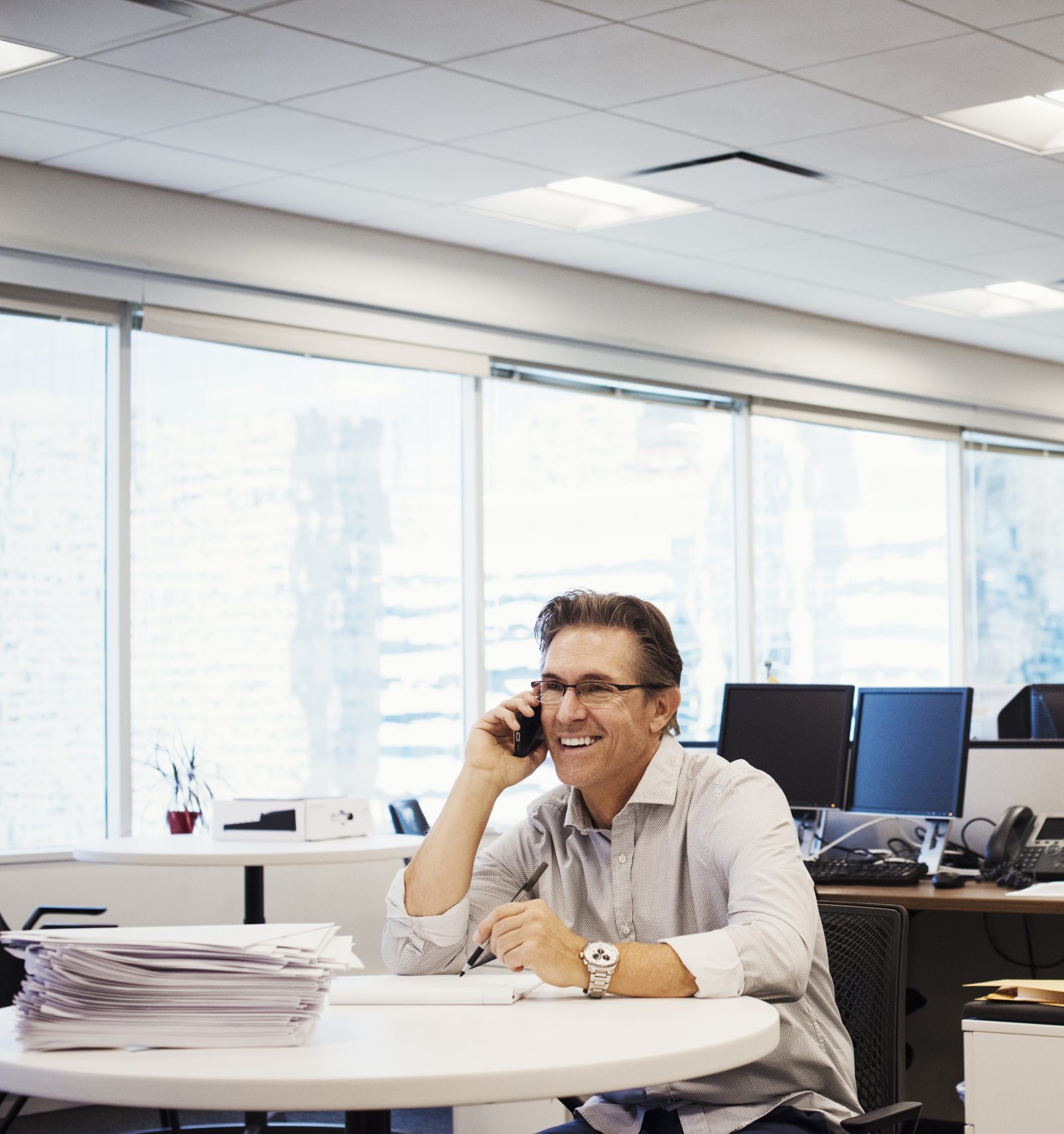 A man sitting at a table in an office, holding a phone to his head and smiling.,New York Business