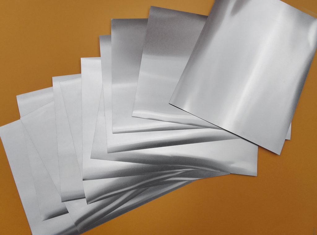 a bunch of square aluminum on yellow cardboard. pile of thin metal industrial materials. square cut set